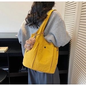 Detail of yellow canvas tote bag with multiple snap pockets and a bear charm accessory