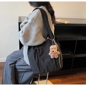 Detail of a large black nylon shoulder bag with a plush dog charm and side pocket