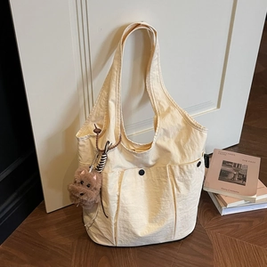Minimalist beige nylon tote bag with multi-pockets and a cute bear charm on a wood floor
