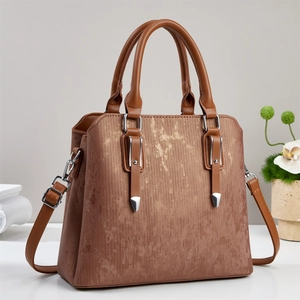 Detail of tan handbag featuring vertical texture, dual handles and adjustable shoulder strap