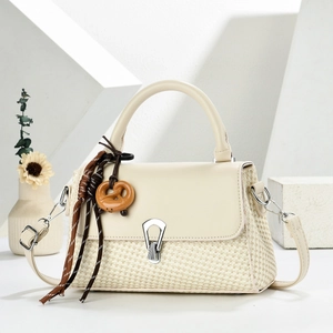 Detail of a beige woven crossbody bag featuring a wooden pretzel charm on the handle