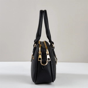 Detail view of black lychee grain leather handbag showing gold zippers and side compartments