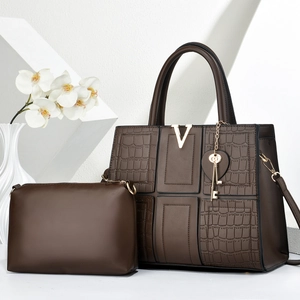 Detail of dark brown crocodile embossed tote bag with gold V-shaped metal logo and charms