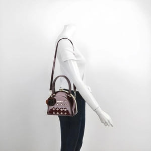 Detail view of burgundy patent leather shell bag with metal studs and flower charm