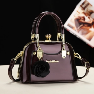 Detail of burgundy patent leather handbag with gold hardware and rose pendant charm