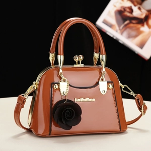 Brown patent leather handbag with a metal frame clasp and decorative rose charm