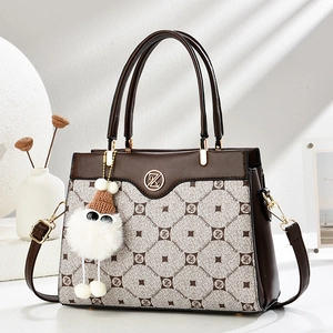 Detail view of coffee and beige tote bag with monogram pattern and white fur ball charm