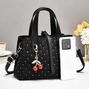 Detail of black quilted handbag with silver rhinestones and a cherry charm next to a phone