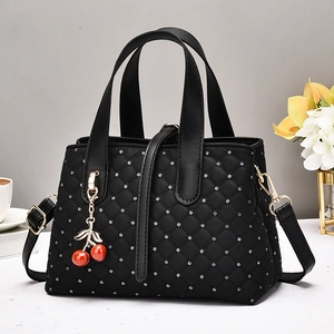 Detail of black quilted handbag with silver polka dots and red cherry charm accessory
