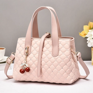 Close-up of pink quilted handbag with red cherry charms and detachable shoulder strap