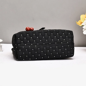 Detail of black quilted nylon handbag featuring red ball clasps and silver studs