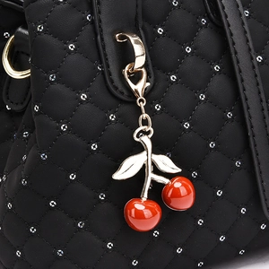 Detailed macro view of black quilted leather handbag with rivets and a cherry charm