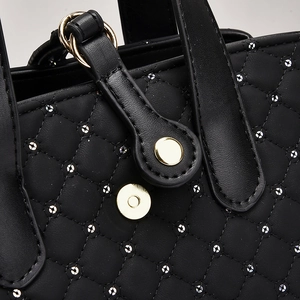 Close-up of black quilted faux leather bag with silver studs and golden metal clasp
