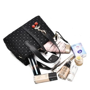 Detailed view of black quilted handbag with silver studs and a cherry pendant