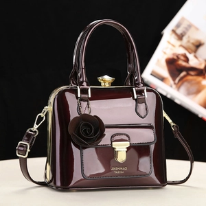 Elegante borsa a mano in vernice bordeaux con chiusura dorata e ciondolo rosa su sfondo studio