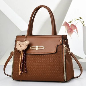 Detail of brown PU leather handbag featuring woven texture and gold hardware with bear charm