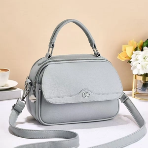 Detail of light gray lychee grain leather handbag with round logo and floral zipper charm