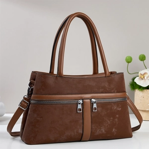Vintage brown crossbody bag with dual handles and side zipper details on white desk