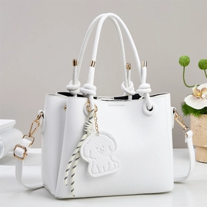 Close-up of white lychee leather handbag with knot handle and dog charm detail
