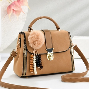 Khaki minimalist handbag with plush ball and wooden bead charms on a soft background