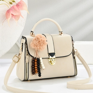 Detail of beige shoulder bag with gold clasp, zipper accents, and colorful bead pendant