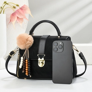 Detail of matte black handbag featuring a golden shield lock and decorative beads