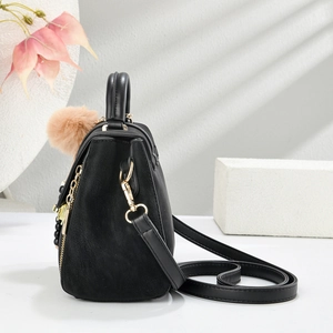 Detail view of black matte leather handbag with golden zipper and plush pendant