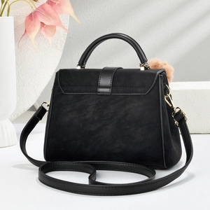 Detail of black trapezoid handbag with matte texture and fuzzy pom-pom charm decoration