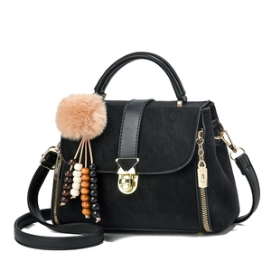 Detail of black matte handbag with gold buckle and fluffy charm accessory on side