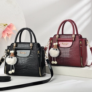 Détail de sacs en cuir verni gaufré crocodile en noir et bordeaux avec pompon en fourrure