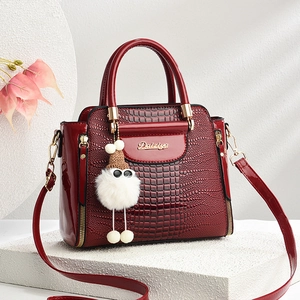 Gros plan d'un sac à main bordeaux motif crocodile avec logo doré et pompon blanc