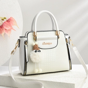 Détail du sac à main blanc motif crocodile avec logo doré et charmant pompon en peluche