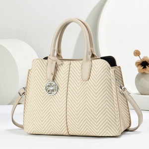 Detail der gewebten Stroh-Tasche mit Chevron-Struktur und Lederbesatz mit Metallanhänger