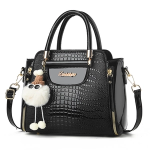 Borsa nera in rilievo coccodrillo con logo dorato e ciondolo in peluche su sfondo bianco
