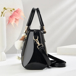 Détail d'un sac à main noir verni avec finitions dorées et un porte-clé pompon en peluche