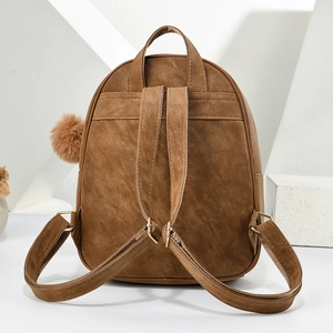 Detail of a brown suede backpack with a plush ball charm and gold-toned metal hardware