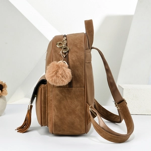 Detail shot of brown frosted leather backpack with plush ball charm and tassel accessories