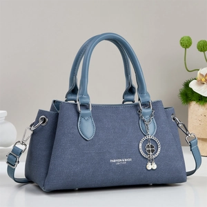 Sac à main trapèze bleu en denim avec pendentif trèfle et poignées en cuir élégantes