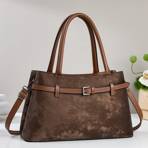 Brown vintage leather tote bag with top handles and adjustable strap on a minimalist desk