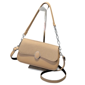 Beige crossbody bag with textured fabric flap and silver oval buckle on a stand