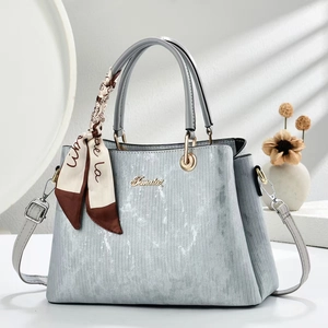 Close-up of light blue textured handbag with gold logo and printed silk scarf handle