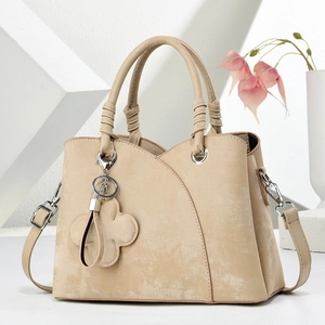 Détail du sac à main beige avec breloque trèfle et poignée décorative élégante
