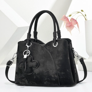 Détail du sac à main noir en daim avec coutures diagonales et breloque trèfle argentée