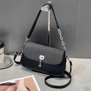 Détail d'un sac sous le bras noir avec rabat texturé et bandoulière en chaîne argentée