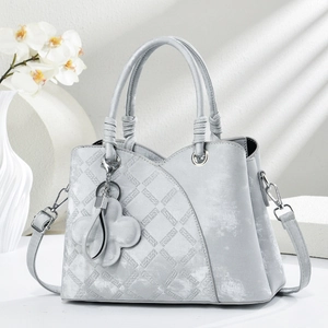 Elegant light gray tote bag with quilted texture and clover charm in soft window light