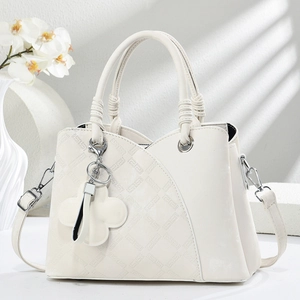 Detail of white crossbody bag featuring asymmetric quilted texture and clover charm