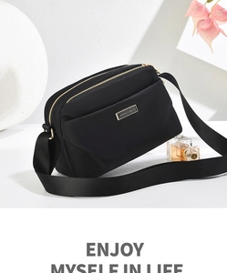 Close-up of black nylon crossbody bag with gold zippers and metal brand logo plate