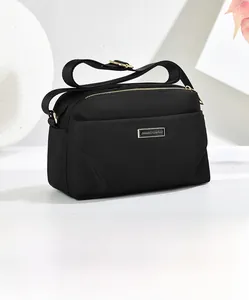 Detail of black nylon crossbody bag featuring triple-zipper design and golden hardware plate