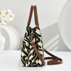 Detail view of jacquard printed handbag with brown leather handle and gold hardware