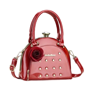 Elegant red patent leather handbag with gold studs and a 3D rose charm on white background